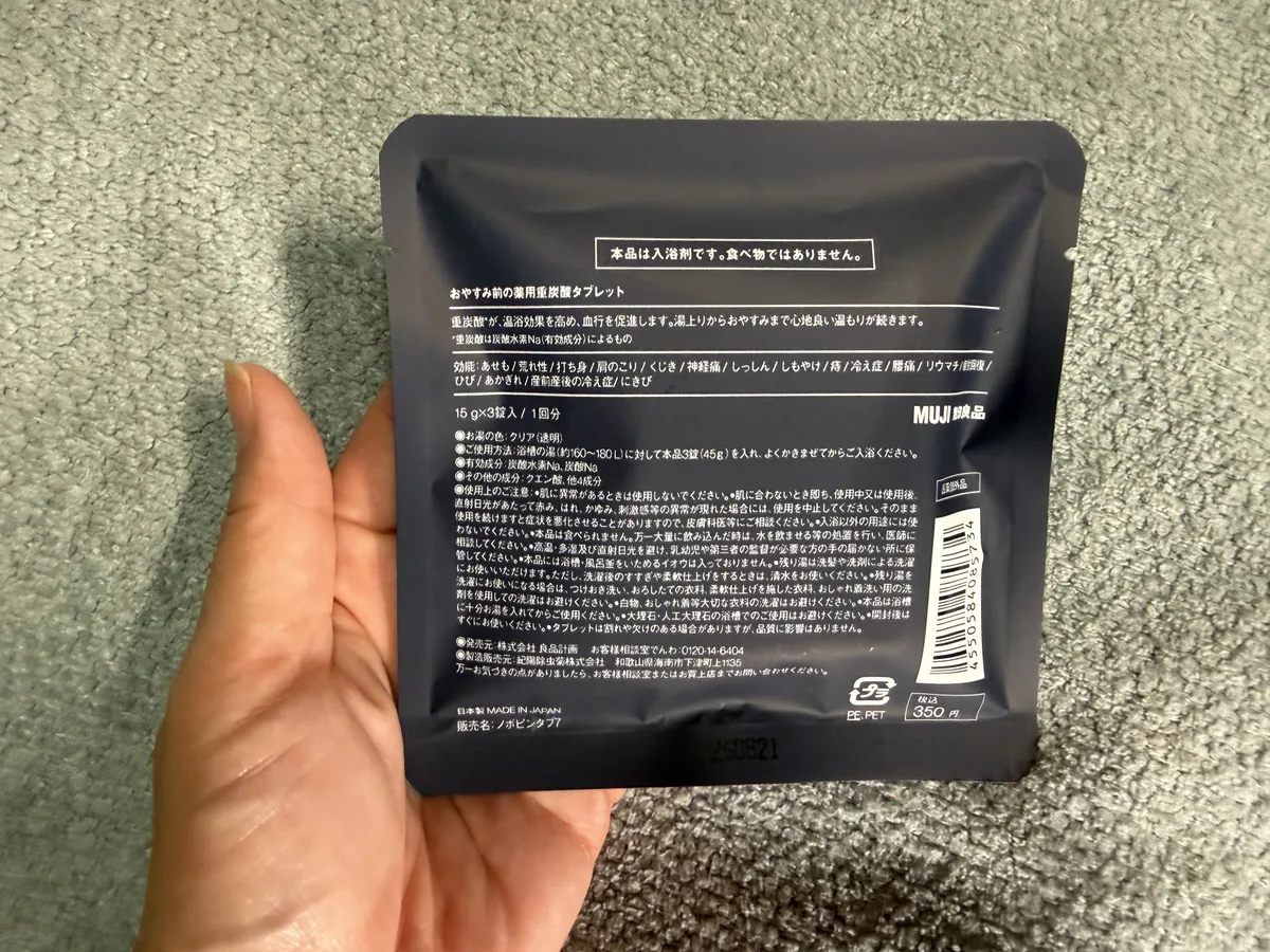 手に持った無印良品のおやすみ前の薬用重炭酸タブレットの分包の裏。成分・発売元・製造販売元の表示